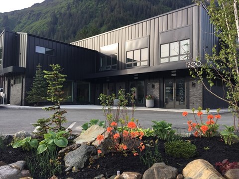 A modern building with a black and grey exterior and a garden in front.
