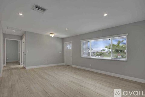 A spacious room with wooden flooring and a window with blinds.