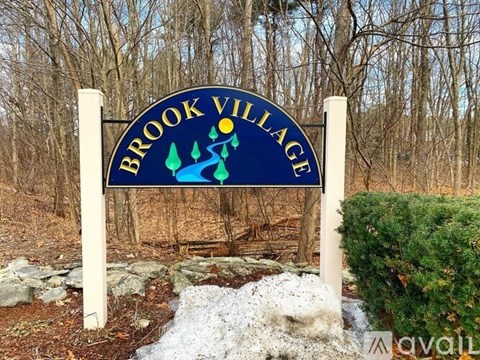 A sign that says Brook Village stands in front of a forest.
