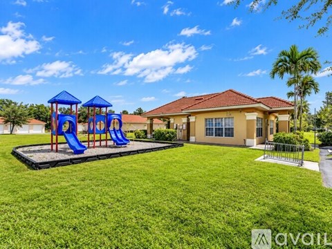 A playground with a blue slide and a yellow house in the background.