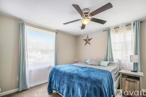A bedroom with a bed, a ceiling fan, and a window with curtains.