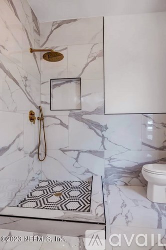 A bathroom with marble tiles and a gold shower head.