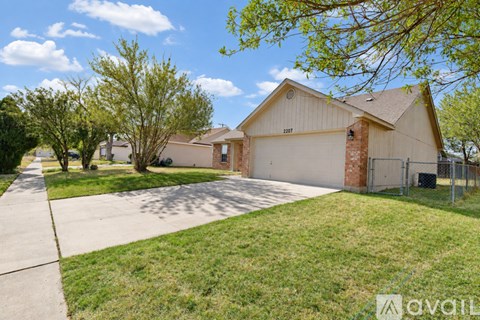 A house with a garage is surrounded by a grassy area and trees.