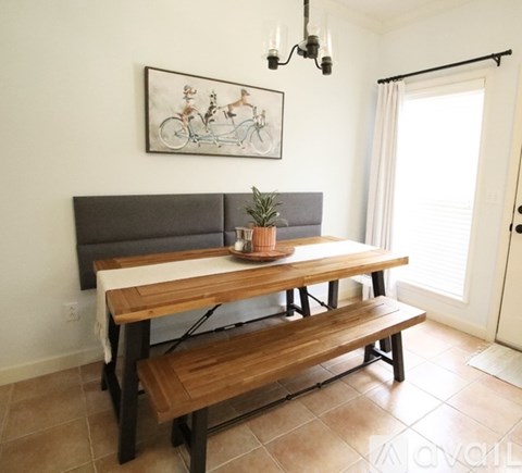 A wooden table with a bench in front of a window with a painting hanging on the wall.