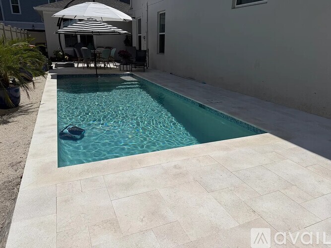 A pool with a white umbrella and chairs.