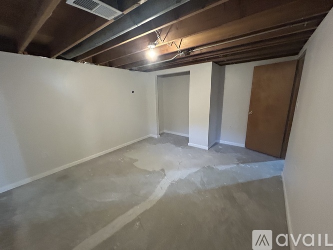 A room with a white wall and a brown door is available for rent.