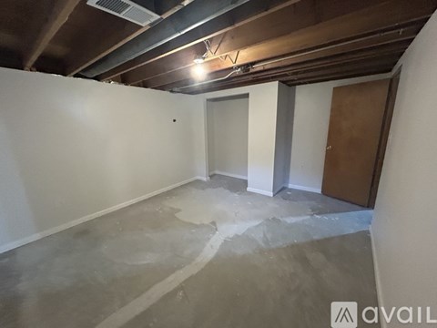 A room with a white wall and a brown door is available for rent.