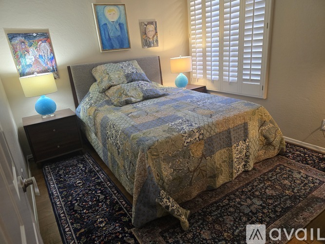 A bedroom with a bed covered in a patterned blanket and two blue lamps on side tables.