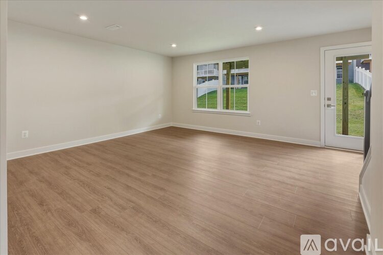 A spacious room with wooden flooring and a view of a fence and greenery outside through a window.