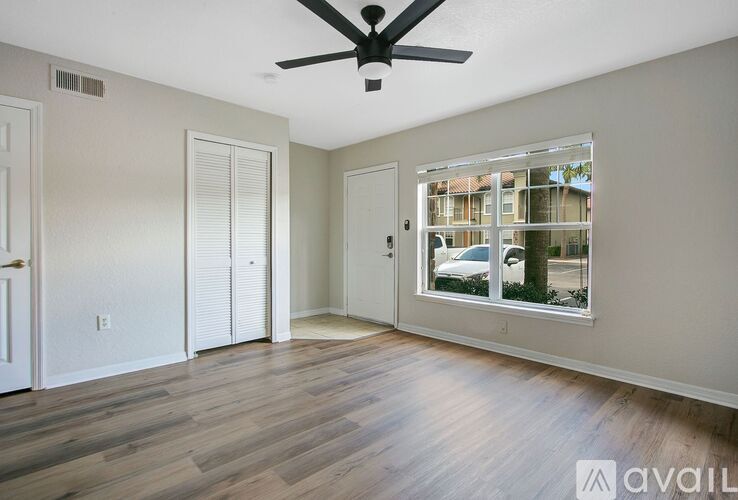A room with a ceiling fan and a window showing a view of a house and trees.