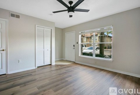 A room with a ceiling fan and a window showing a view of a house and trees.