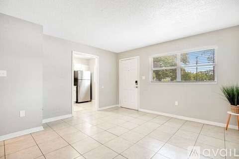 A spacious room with a door leading to another room and a window with a view of trees outside.