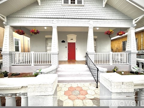 A white house with a red door and flower pots on the porch.