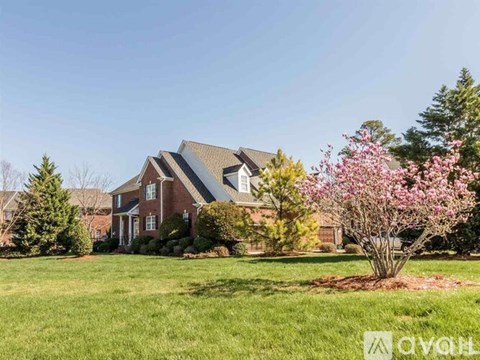 A house with a red brick exterior and a large front yard with a flowering tree.