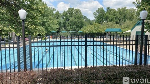 A pool surrounded by a black fence with a green umbrella in the background.