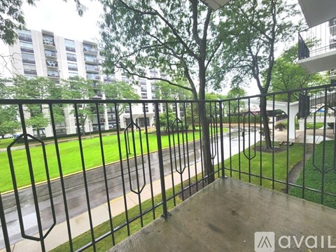 A balcony with a metal railing overlooks a green lawn and apartment buildings.