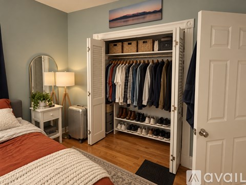 A bedroom with a large open closet and a bed with a white knitted blanket.