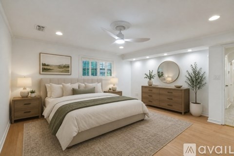 A well-lit bedroom with a large bed, a side table with a lamp, and a dresser with a mirror.