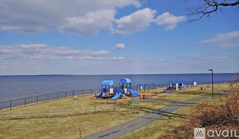A playground with a blue slide and a wooden bench is located near a body of water.