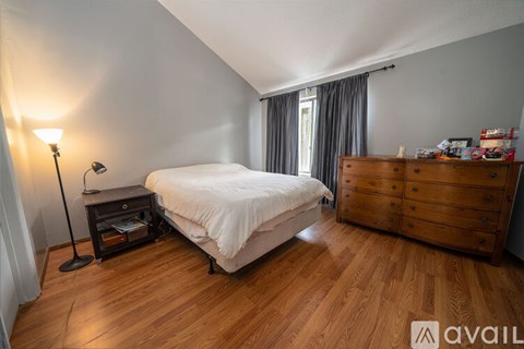 A bedroom with a bed, nightstand, and wooden floors.