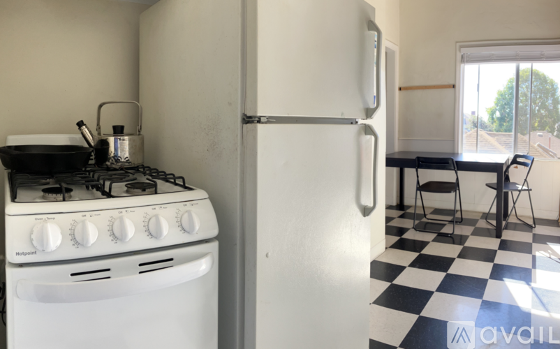 A white gas stove with a pot on it and a white fridge in a kitchen with a black and white checkered floor.