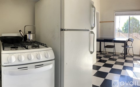 A white gas stove with a pot on it and a white fridge in a kitchen with a black and white checkered floor.