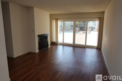 A room with wooden floors and a fireplace with a view of a pool outside.
