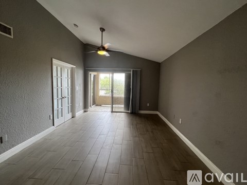 A spacious room with a ceiling fan and sliding glass doors leading to a balcony.