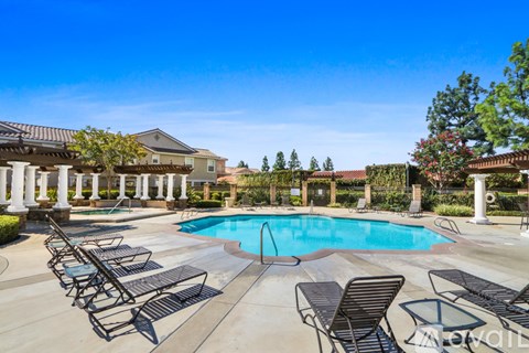 A pool surrounded by chairs and pillars with a house in the background.