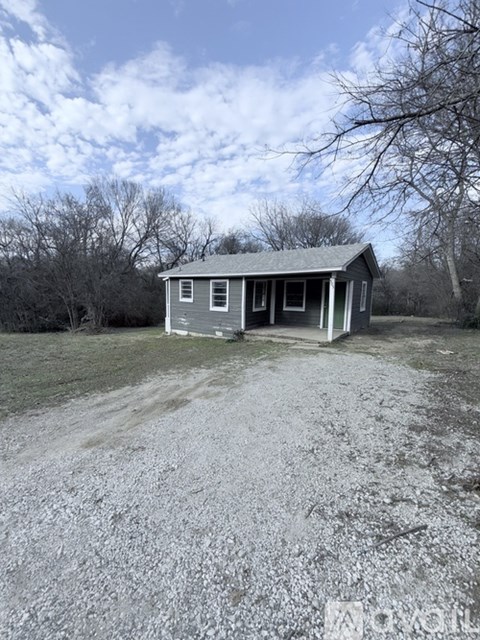 A small house with a gravel driveway in front of it.