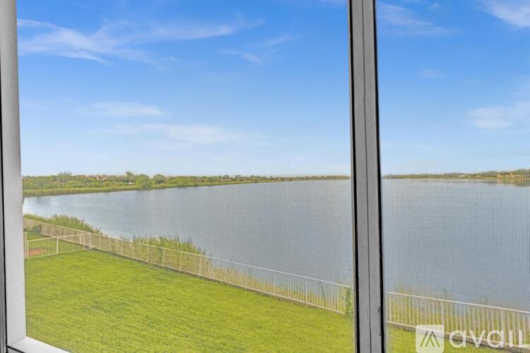 A view from a window looking out at a grassy field and a body of water.