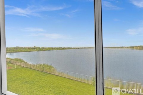A view from a window looking out at a grassy field and a body of water.