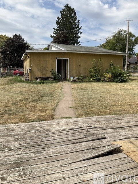 A wooden building with a heart on the side is surrounded by grass.