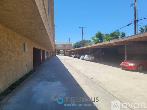 A red car is parked in a parking lot with a building on the left side.