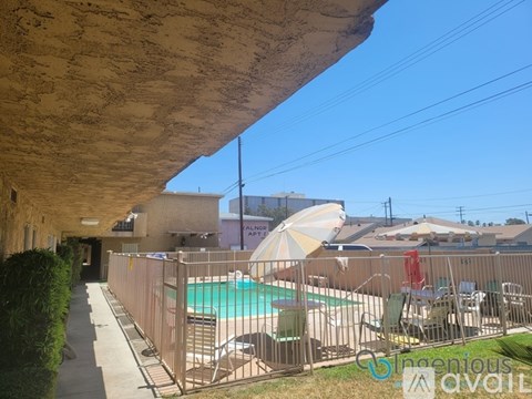 A pool area with a fence and chairs under a shaded area.