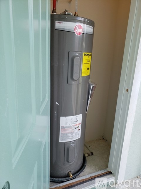 A water heater is installed in a narrow space between a door and a wall.