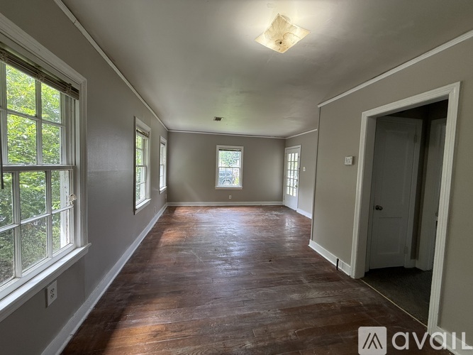 A room with wooden floors and white walls, with a window on the left and a door on the right.