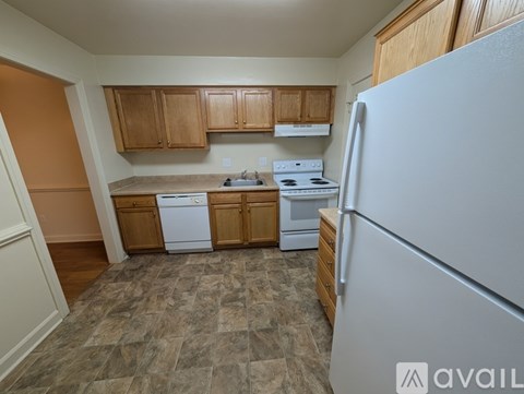 A kitchen with a white refrigerator, wooden cabinets, and a tiled floor.