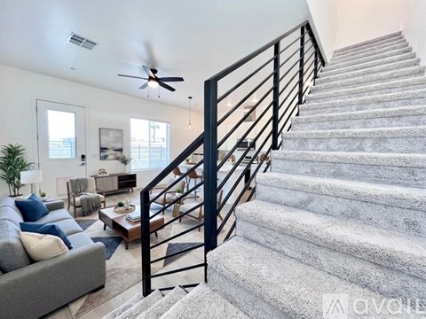 A staircase with a metal railing leads up to a living room with a couch and a ceiling fan.