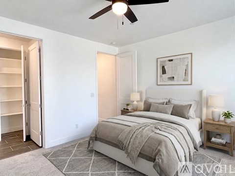 A bedroom with a bed, a ceiling fan, and a nightstand with a lamp.