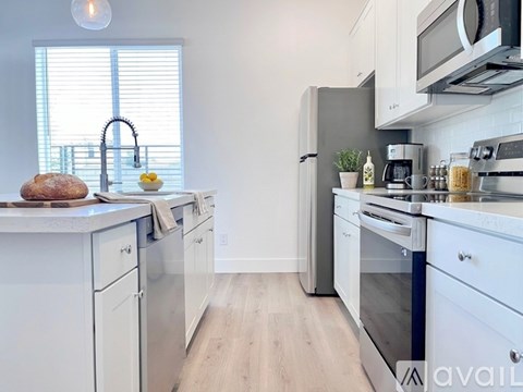 A kitchen with white cabinets and appliances, a window with blinds, and a wooden floor.