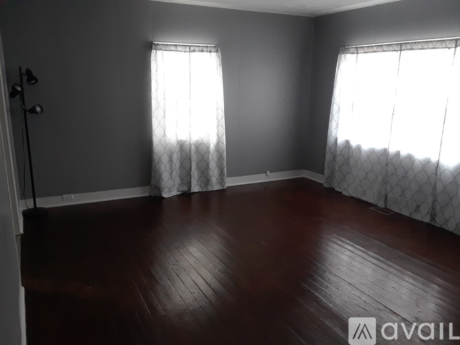 A room with wooden floors and two windows with curtains.