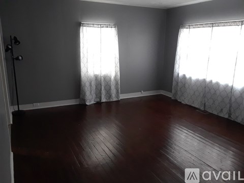 A room with wooden floors and two windows with curtains.