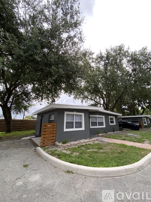 A small house with a grey exterior and a brown door is surrounded by trees.
