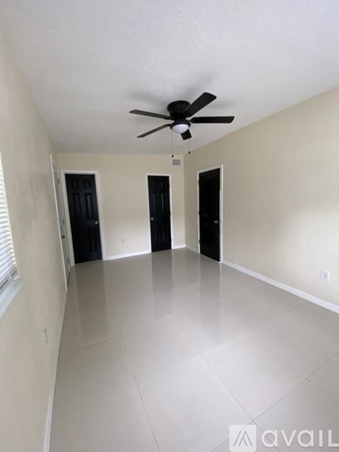 A spacious room with a ceiling fan and three doors.