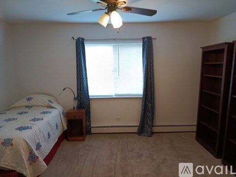 A bedroom with a bed, a ceiling fan, and a window with curtains.