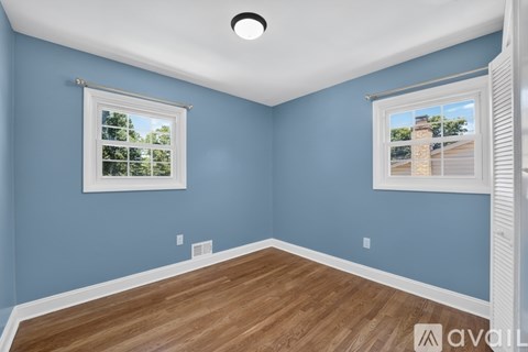 A room with blue walls and wooden flooring, featuring a window with a view of a tree and a building outside.