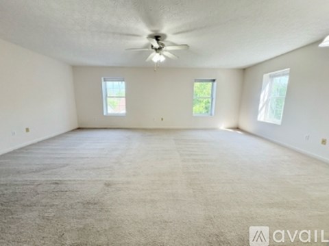 A spacious room with a carpeted floor and a ceiling fan.