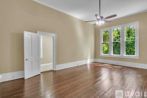 A room with a ceiling fan and a window with a view of trees.