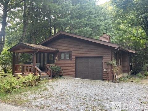 A house with a brown roof and a garage is surrounded by trees.